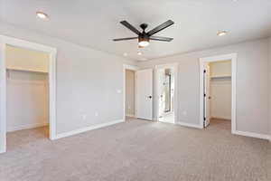 Unfurnished bedroom featuring light carpet, ensuite bathroom, a spacious closet, and ceiling fan