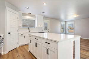 Kitchen featuring white cabinets, sink, light wood-type flooring, tasteful backsplash, and a kitchen island