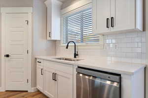 Kitchen with light wood-type flooring, light stone counters, stainless steel dishwasher, sink, and white cabinets