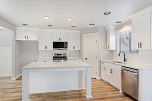 Kitchen featuring white cabinetry, sink, appliances with stainless steel finishes, a kitchen island, and light wood-type flooring