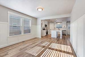 Unfurnished living room featuring sink, a textured ceiling, and light wood-type flooring