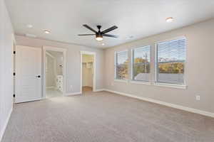 Unfurnished bedroom featuring a walk in closet, a closet, ceiling fan, and light colored carpet