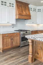 Kitchen with premium range hood, dark wood-type flooring, light stone countertops, stainless steel range, and white cabinetry