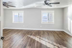 Spare room featuring a textured ceiling, ceiling fan, dark wood-type flooring, and a wealth of natural light