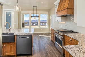 Kitchen featuring light stone countertops, custom range hood, stainless steel appliances, decorative light fixtures, and dark hardwood / wood-style floors