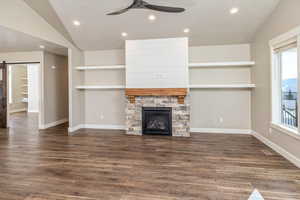 Unfurnished living room featuring a stone fireplace, ceiling fan, dark hardwood / wood-style floors, and vaulted ceiling