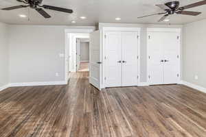 Unfurnished bedroom featuring a textured ceiling, ceiling fan, dark wood-type flooring, and multiple closets