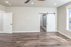 Spare room with a barn door, ceiling fan, and dark hardwood / wood-style floors