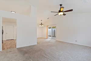 Carpeted empty room with ceiling fan with notable chandelier and high vaulted ceiling