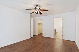 Unfurnished bedroom with a walk in closet, dark hardwood / wood-style floors, ceiling fan, connected bathroom, and a closet