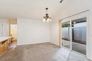 Carpeted empty room featuring lofted ceiling and an inviting chandelier