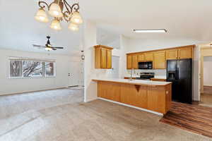 Kitchen with hanging light fixtures, kitchen peninsula, light colored carpet, vaulted ceiling, and black appliances