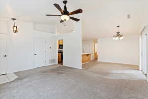 Unfurnished living room with light carpet, ceiling fan with notable chandelier, high vaulted ceiling, and sink