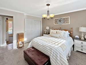 Carpeted bedroom featuring a textured ceiling, a closet, ornamental molding, and a notable chandelier