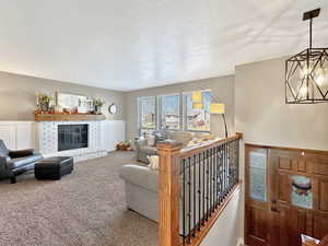 Living room with carpet, a textured ceiling, a brick fireplace, and a chandelier