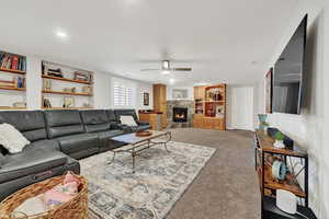 Living room featuring a fireplace, carpet flooring, and ceiling fan