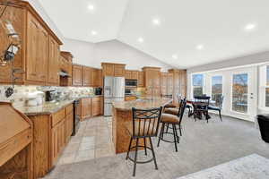 Kitchen featuring stainless steel appliances, lofted ceiling, a breakfast bar area, light carpet, and a center island with sink