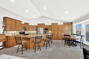 Kitchen featuring light carpet, an island with sink, stainless steel appliances, and lofted ceiling