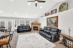 Living room featuring ceiling fan, light colored carpet, a fireplace, and high vaulted ceiling