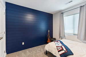 Carpeted bedroom featuring multiple windows, wooden walls, and a textured ceiling