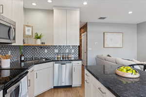 Kitchen featuring appliances with stainless steel finishes, tasteful backsplash, dark stone counters, sink, and light hardwood / wood-style floors