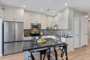 Kitchen featuring dark stone counters, sink, light hardwood / wood-style flooring, tasteful backsplash, and stainless steel appliances