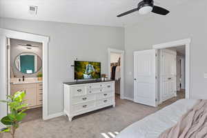 Bedroom featuring ensuite bathroom, light colored carpet, ceiling fan, a spacious closet, and lofted ceiling