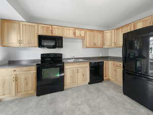 Kitchen with light brown cabinets, sink, and black appliances