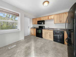 Kitchen with light brown cabinetry, black appliances, and sink