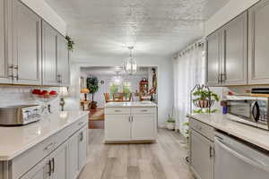 Kitchen with stainless steel appliances, light hardwood / wood-style floors, decorative light fixtures, gray cabinets, and decorative backsplash