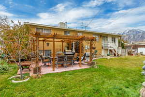 Rear view of house featuring a pergola, an outdoor fire pit, a patio area, a mountain view, and a yard