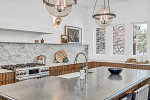 Kitchen with decorative backsplash, high end stove, sink, decorative light fixtures, and a center island