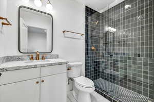 Bathroom with tiled shower, tile patterned floors, vanity, and toilet