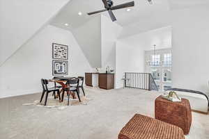 Carpeted dining room with ceiling fan with notable chandelier and lofted ceiling