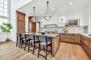 Kitchen featuring light hardwood / wood-style flooring, an island with sink, pendant lighting, a kitchen bar, and decorative backsplash