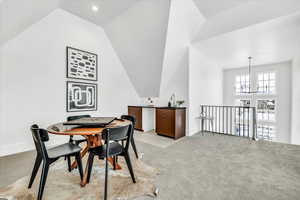 Dining area featuring lofted ceiling, light carpet, and an inviting chandelier