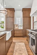 Kitchen featuring custom exhaust hood, decorative light fixtures, high end stainless steel range, light wood-type flooring, and a notable chandelier