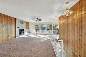 Unfurnished living room featuring wood walls, ceiling fan with notable chandelier, a textured ceiling, a fireplace, and carpet floors