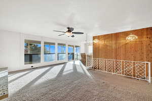 Carpeted spare room featuring a textured ceiling, ceiling fan with notable chandelier, and wooden walls