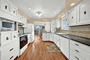 Kitchen with sink, a chandelier, light hardwood / wood-style floors, white appliances, and white cabinets