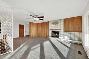 Unfurnished living room with carpet, ceiling fan, wood walls, and a brick fireplace