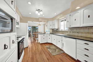 Kitchen with white cabinetry, light hardwood / wood-style flooring, a healthy amount of sunlight, and white appliances