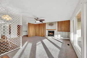 Unfurnished living room with carpet flooring, a brick fireplace, ceiling fan, and wooden walls