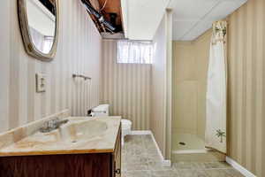 Bathroom featuring walk in shower, a drop ceiling, vanity, tile patterned flooring, and toilet