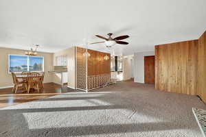 Unfurnished living room featuring ceiling fan with notable chandelier, dark wood-type flooring, and wooden walls