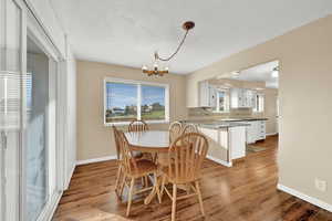 Dining area with a textured ceiling, light wood-type flooring, and a notable chandelier