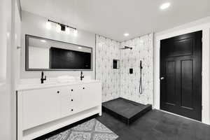 Bathroom featuring tile patterned floors, vanity, a tile shower, and a textured ceiling