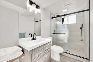 Bathroom featuring wood-type flooring, vanity, a shower with shower door, and toilet