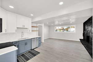 Kitchen with stainless steel dishwasher, sink, a fireplace, light hardwood / wood-style floors, and white cabinetry