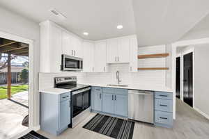 Kitchen featuring light wood-type flooring, a textured ceiling, stainless steel appliances, sink, and white cabinetry